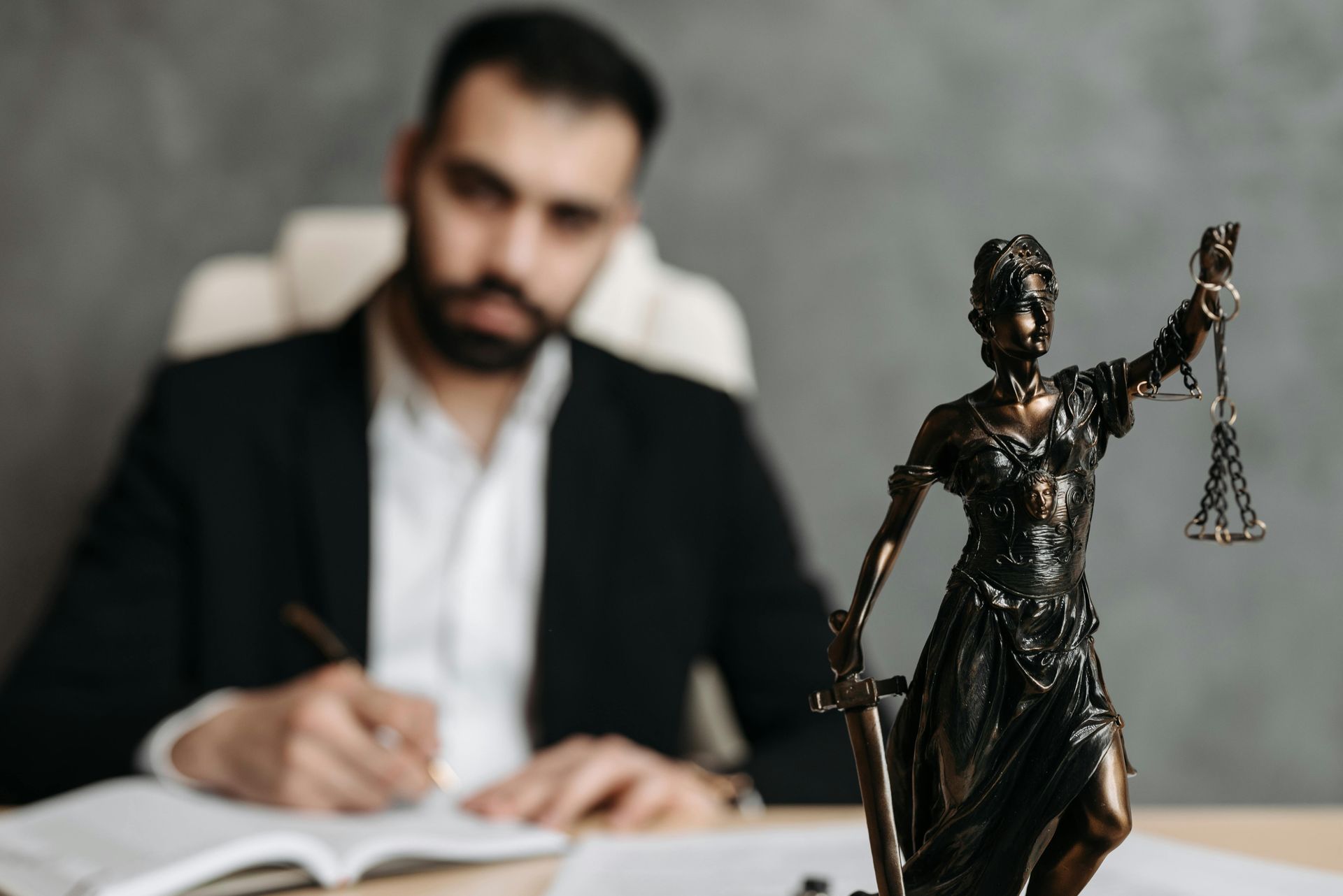 A man is sitting at a desk with a statue of justice in front of him.