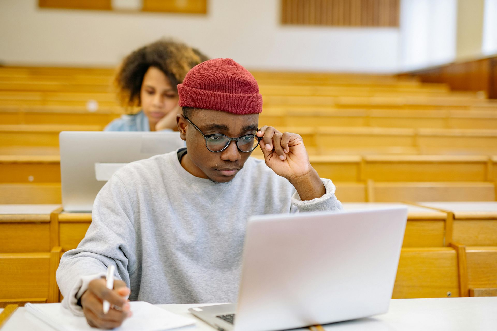A man is sitting in front of a laptop computer in a lecture hall.