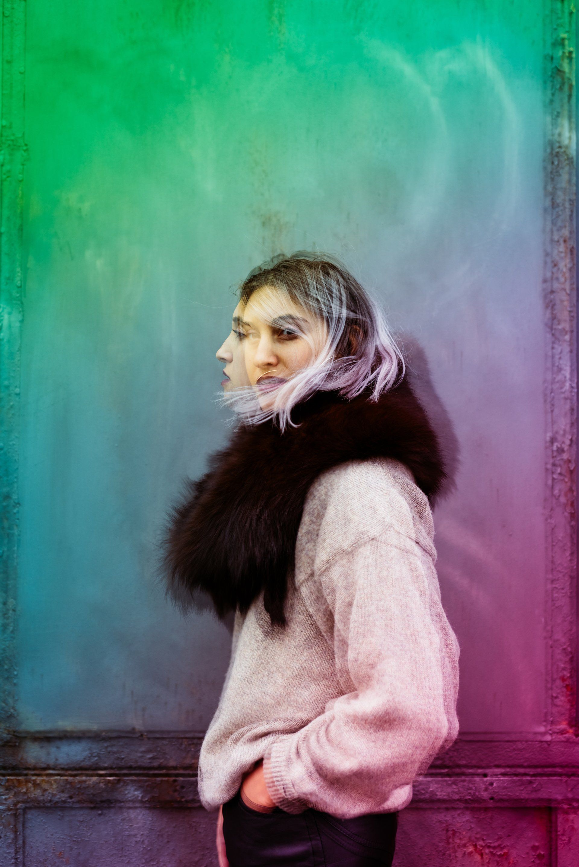 Una mujer que lleva una bufanda de piel y un suéter está parada frente a una pared colorida.