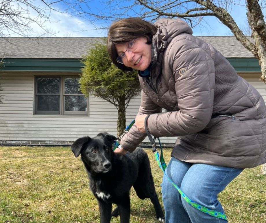 A woman is petting a black dog on a leash in front of a house.