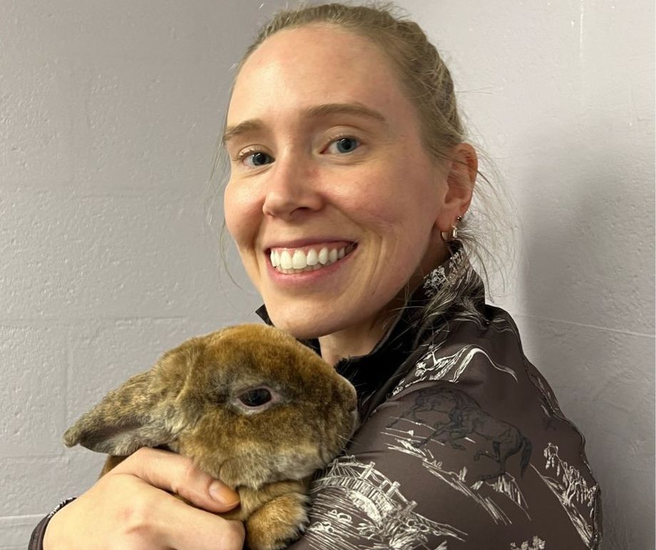 A woman is holding a brown rabbit in her arms and smiling.