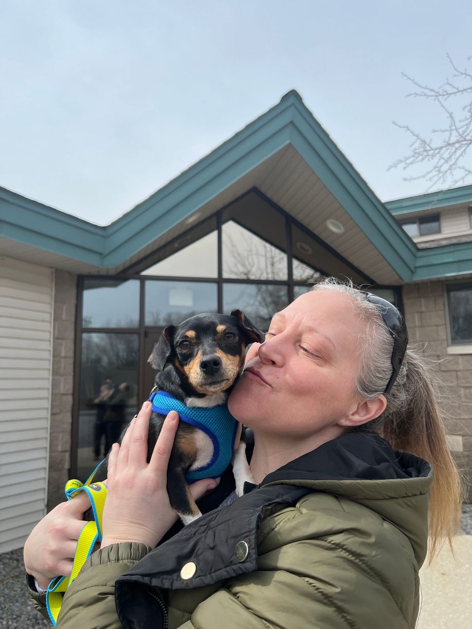 A woman is holding a small dog in front of a building.