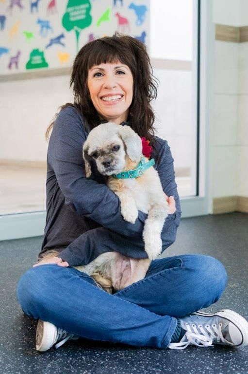 A woman is sitting on the floor holding a small dog.