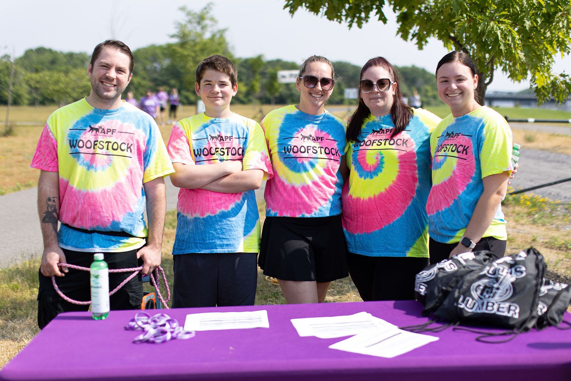 A group of people wearing tie dye shirts are standing around a purple table.