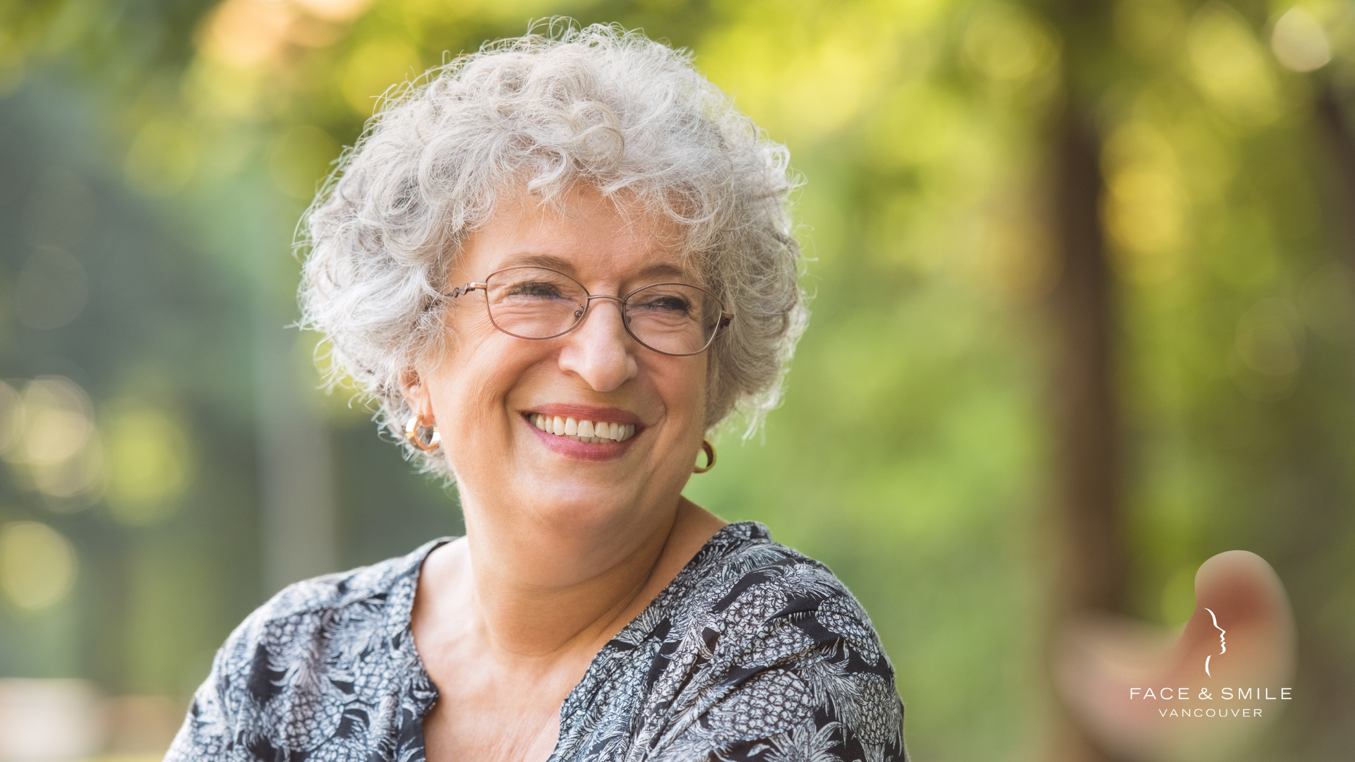 An elderly woman with glasses is smiling for the camera.