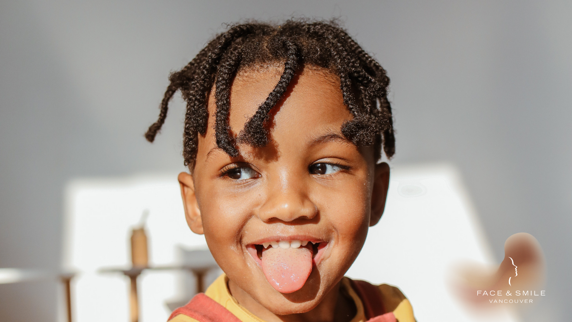 A young boy with dreadlocks is sticking his tongue out.