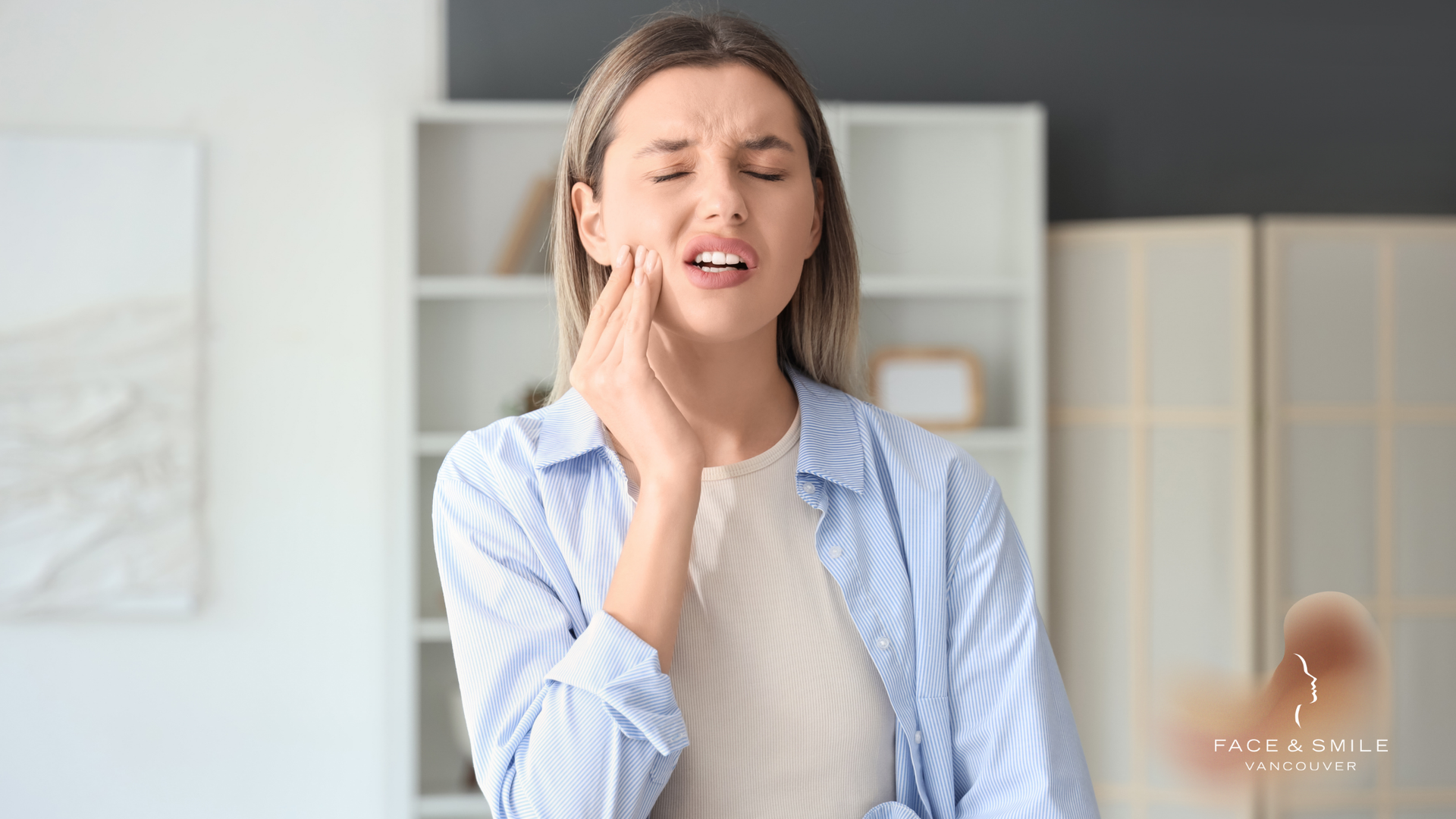 Woman holding jaw, showing pain, inside a room.