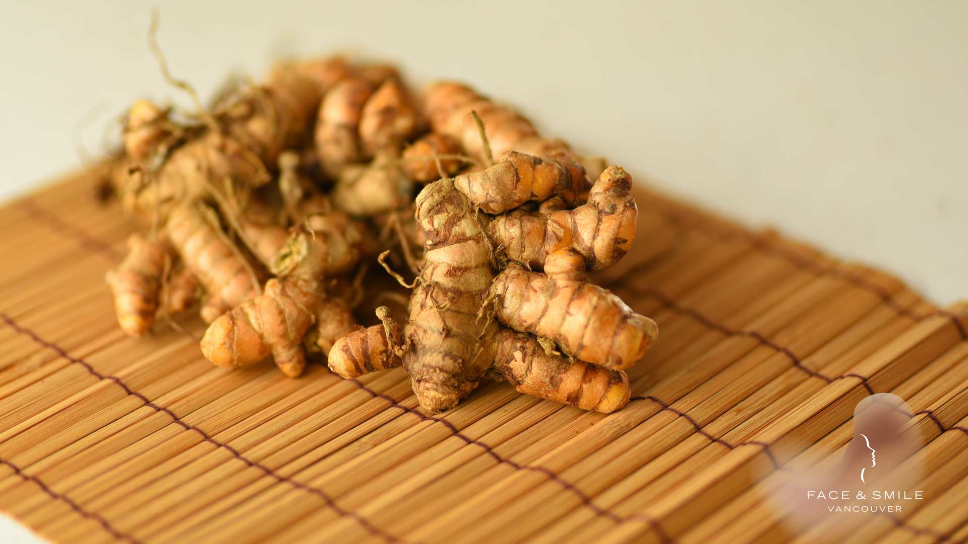 A bunch of turmeric roots are sitting on a bamboo mat.