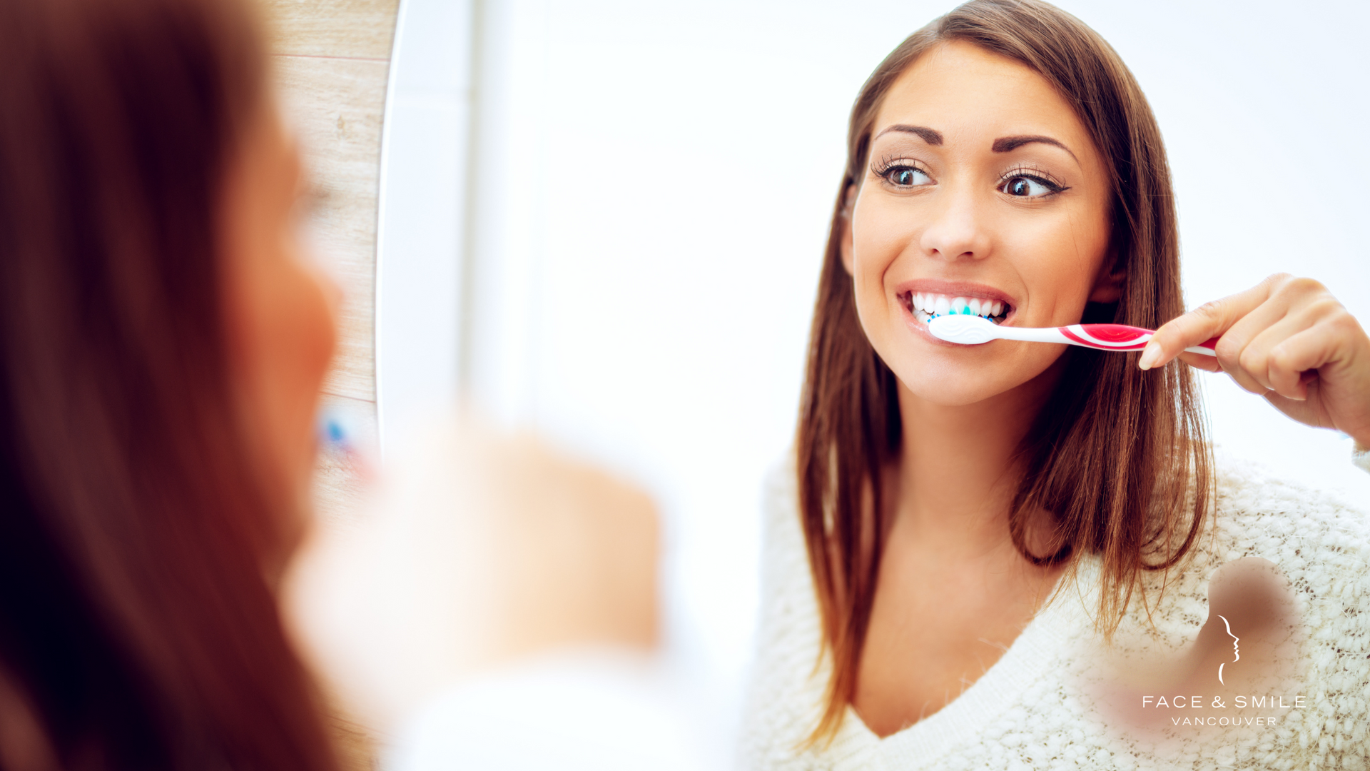 A woman is brushing her teeth in front of a mirror.