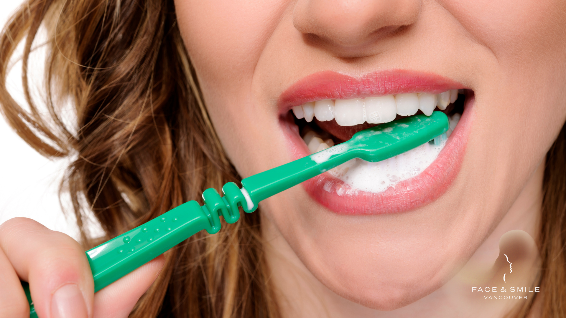 Woman brushing teeth with a green toothbrush, mouth open, white foam visible.