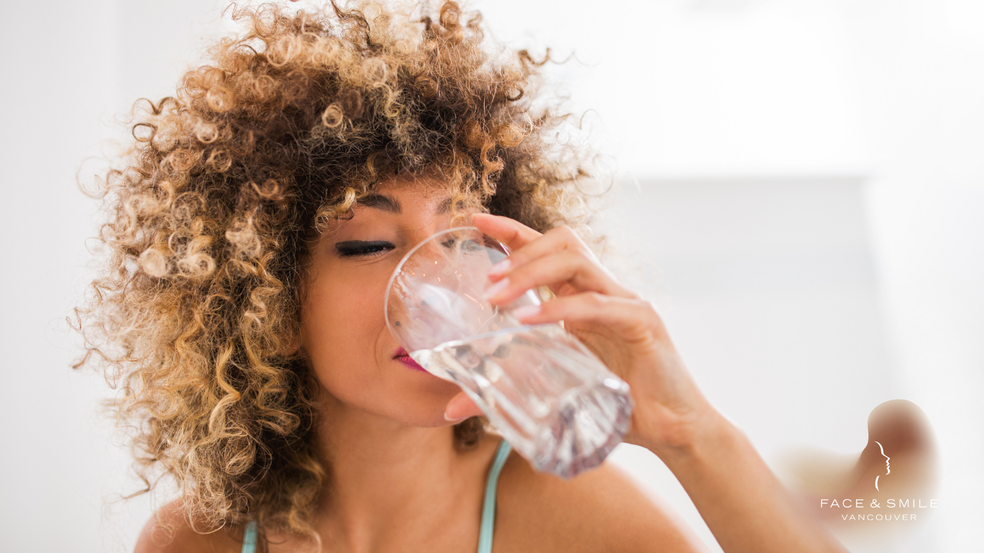 A woman with curly hair is drinking a glass of water.