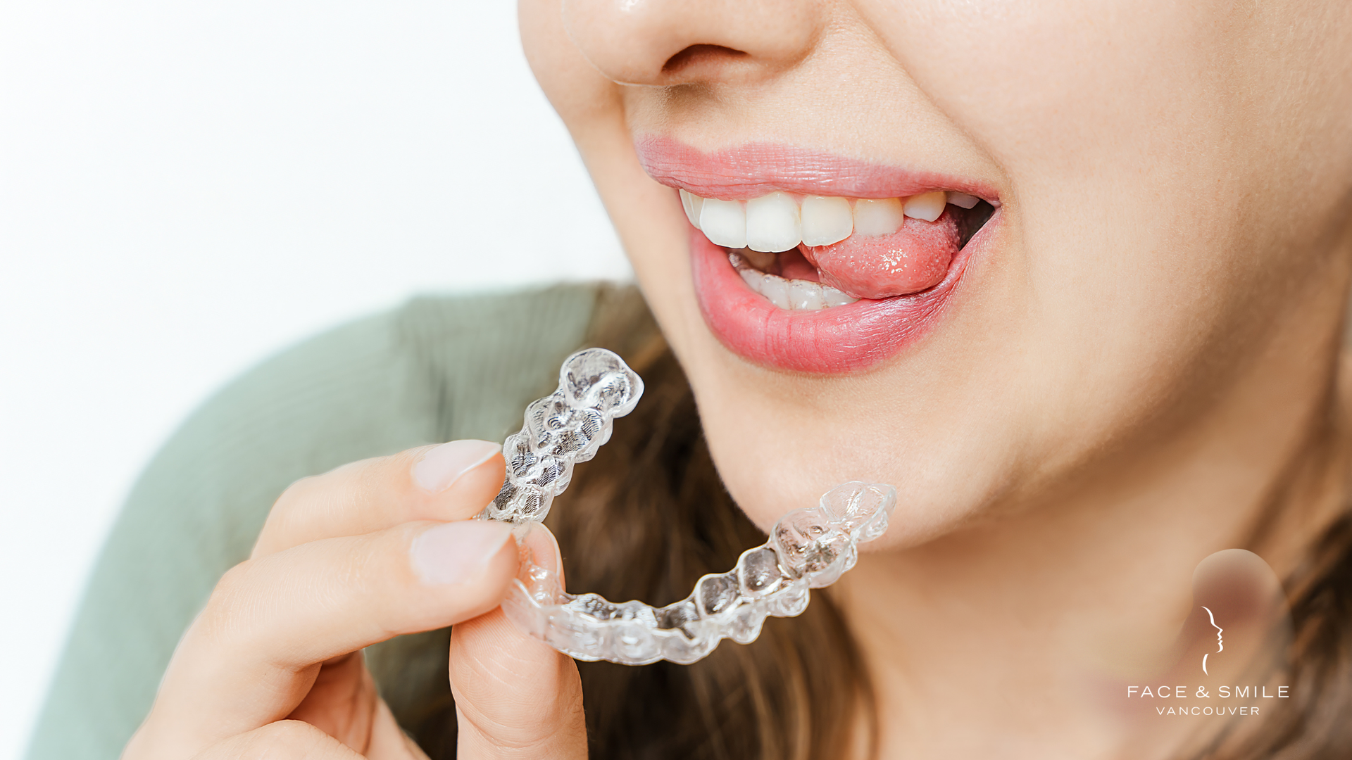Person holding clear aligner, smiling, preparing to put it in mouth.