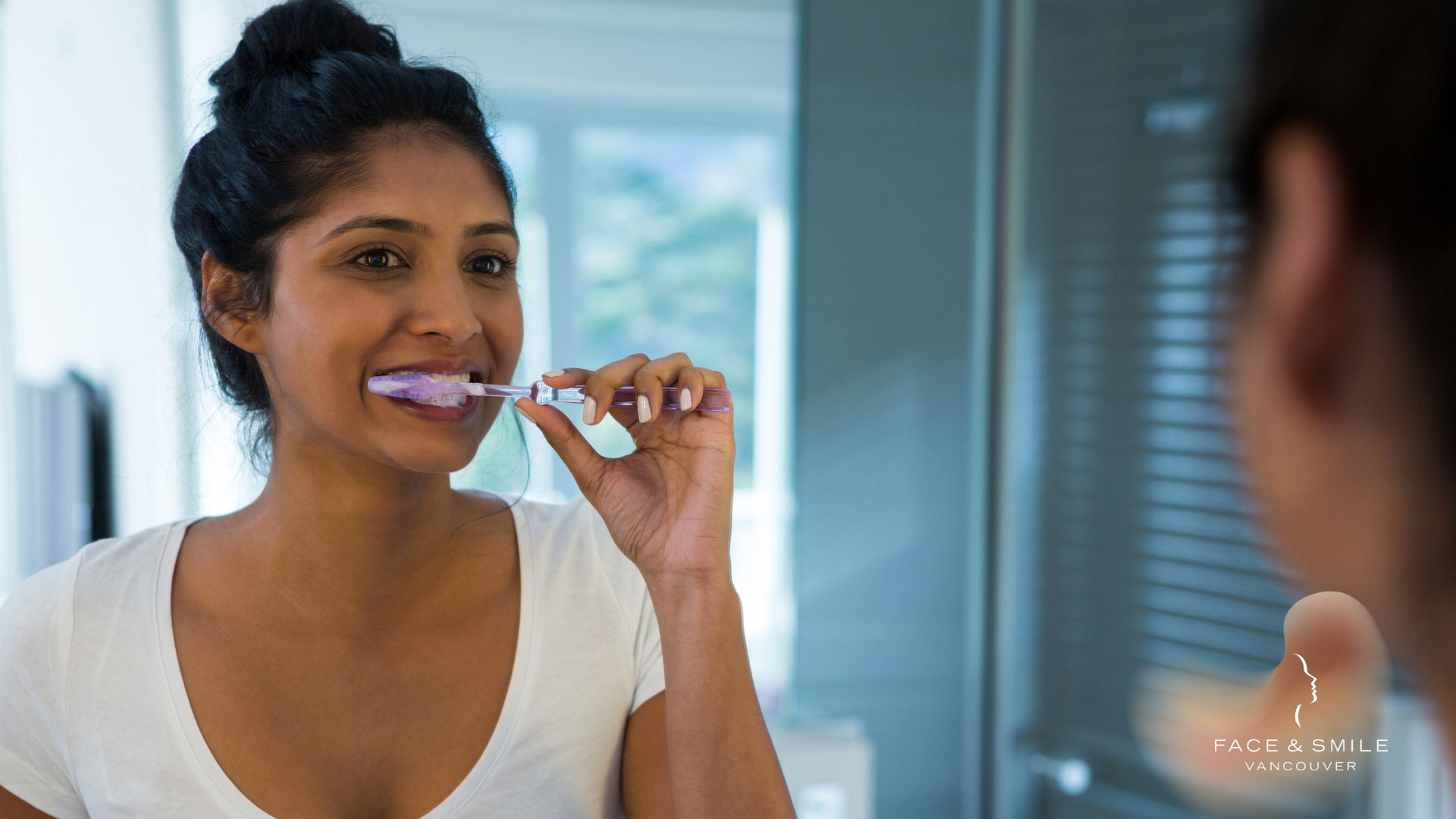 A woman is brushing her teeth in front of a mirror.
