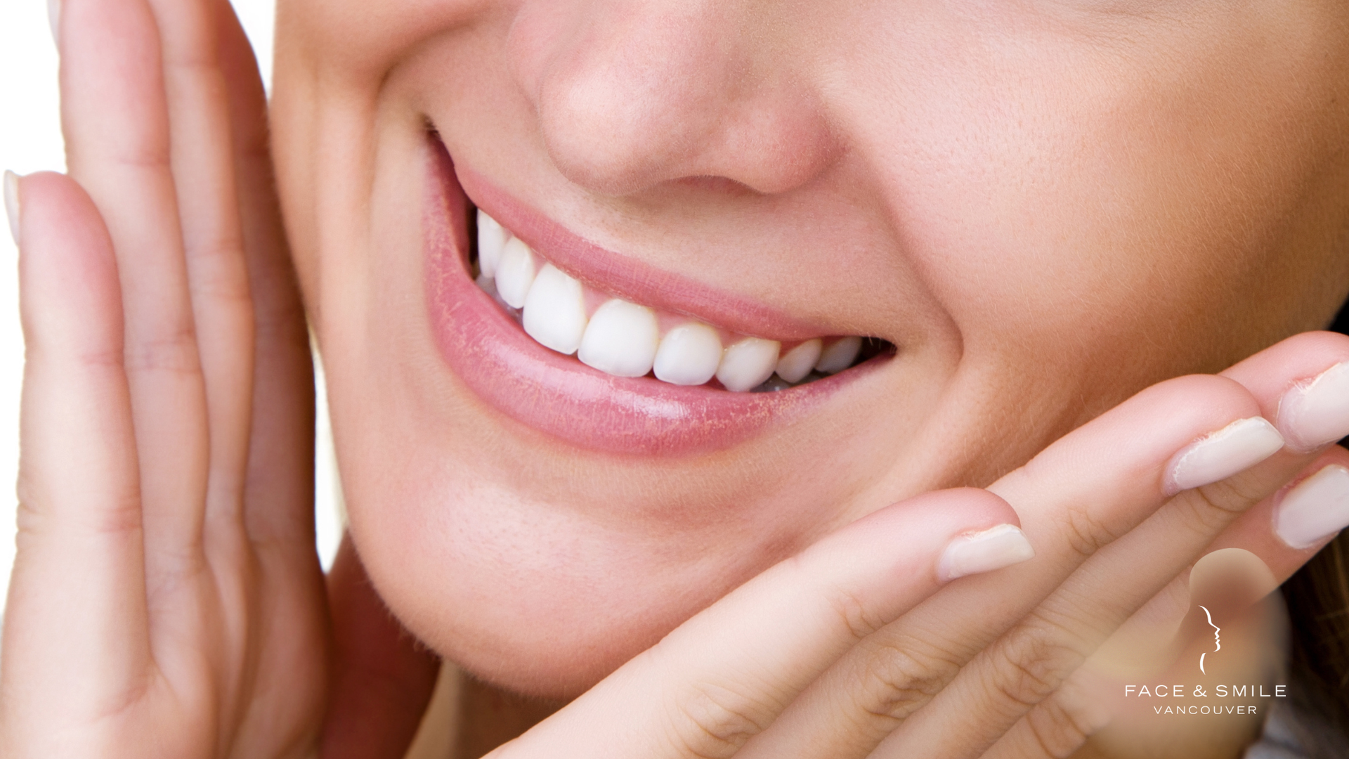 Smiling mouth with bright white teeth, hands framing face, light skin, close-up.