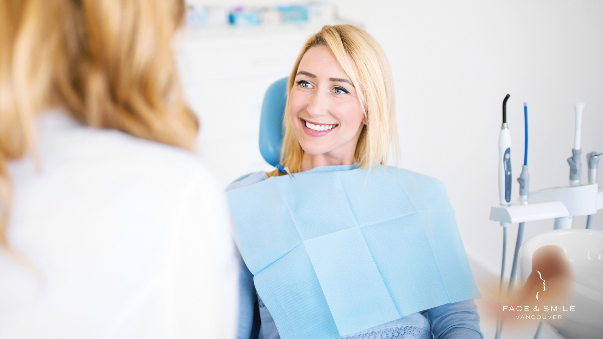 A woman is smiling while sitting in a dental chair.