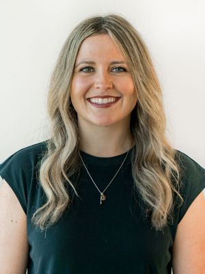 A woman wearing a black shirt and a necklace is smiling for the camera.