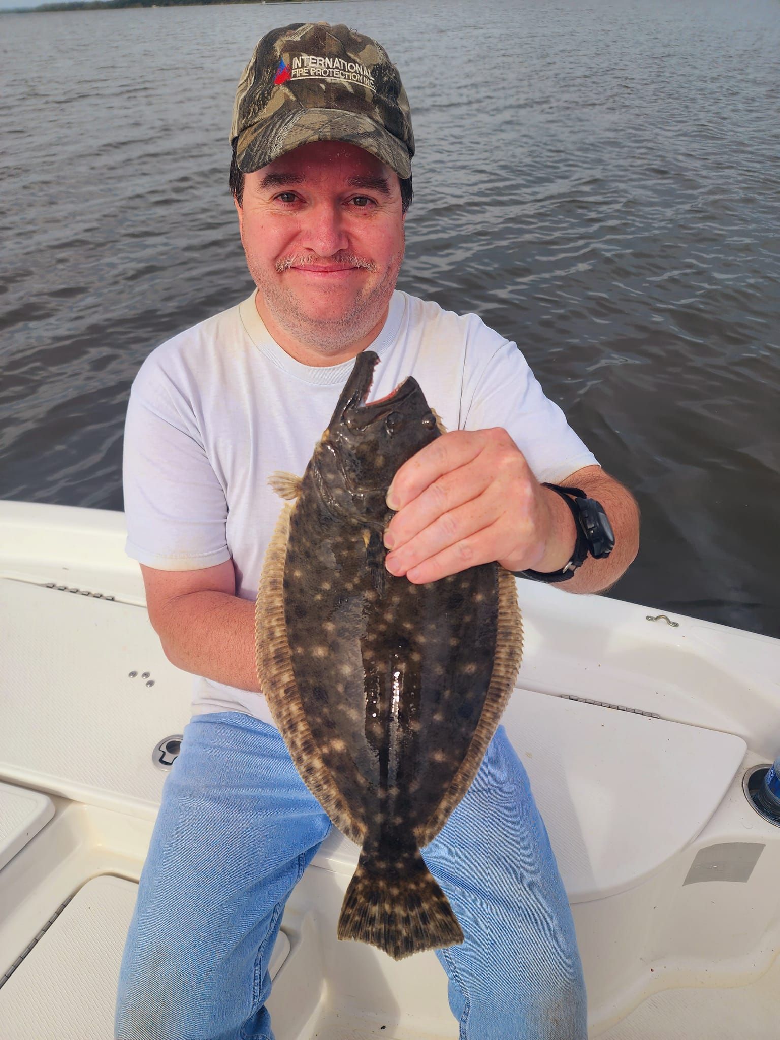 Man holding a flat fish on a boat, smiling; water in background.