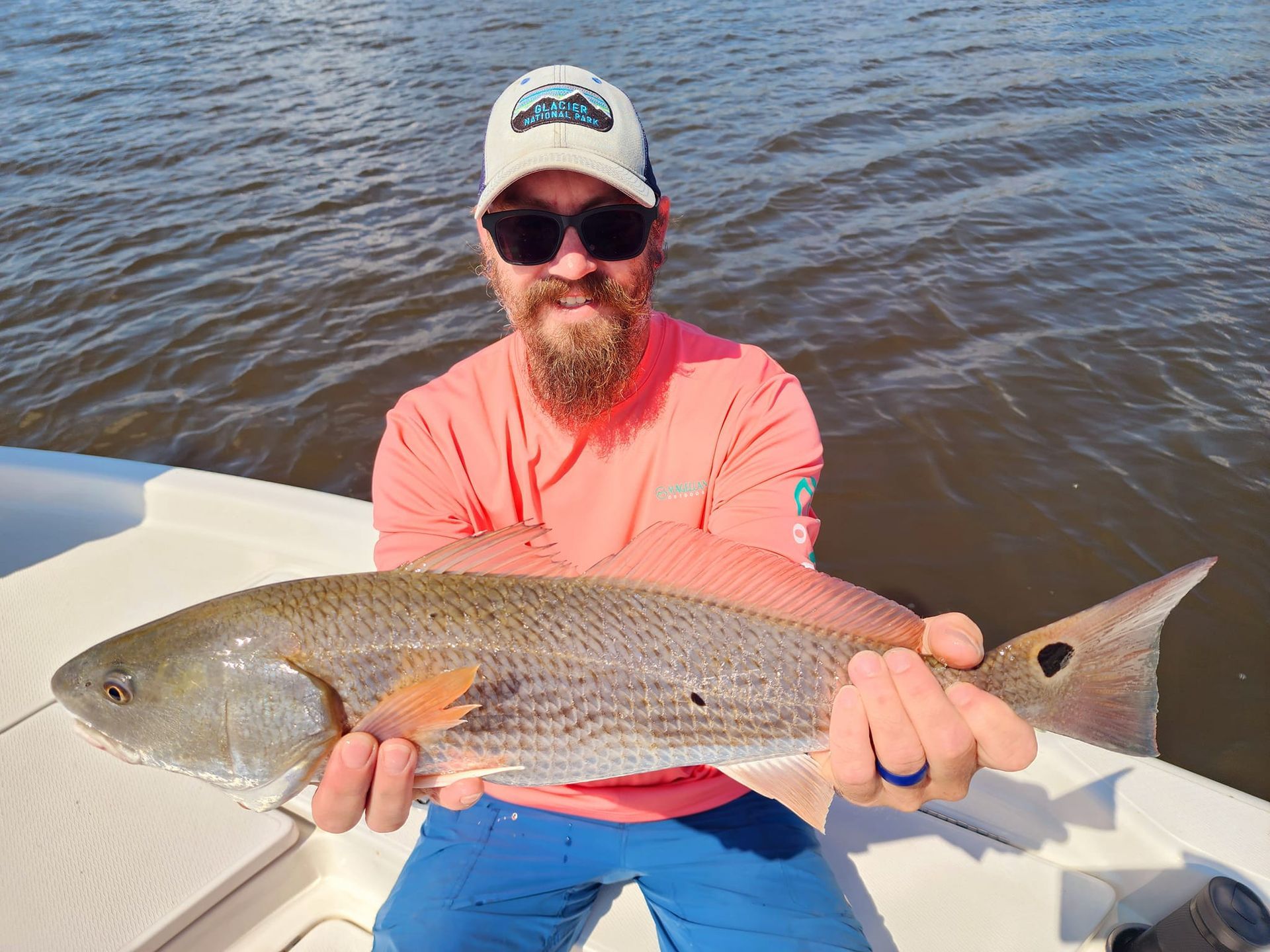 Man holding a large redfish on a boat; water in background. He's smiling.
