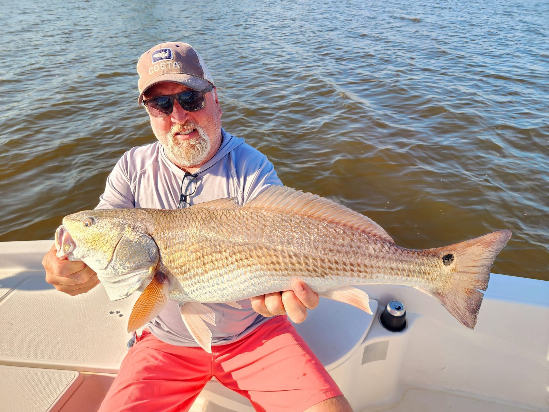 Man holding a large redfish on a boat; water in background.