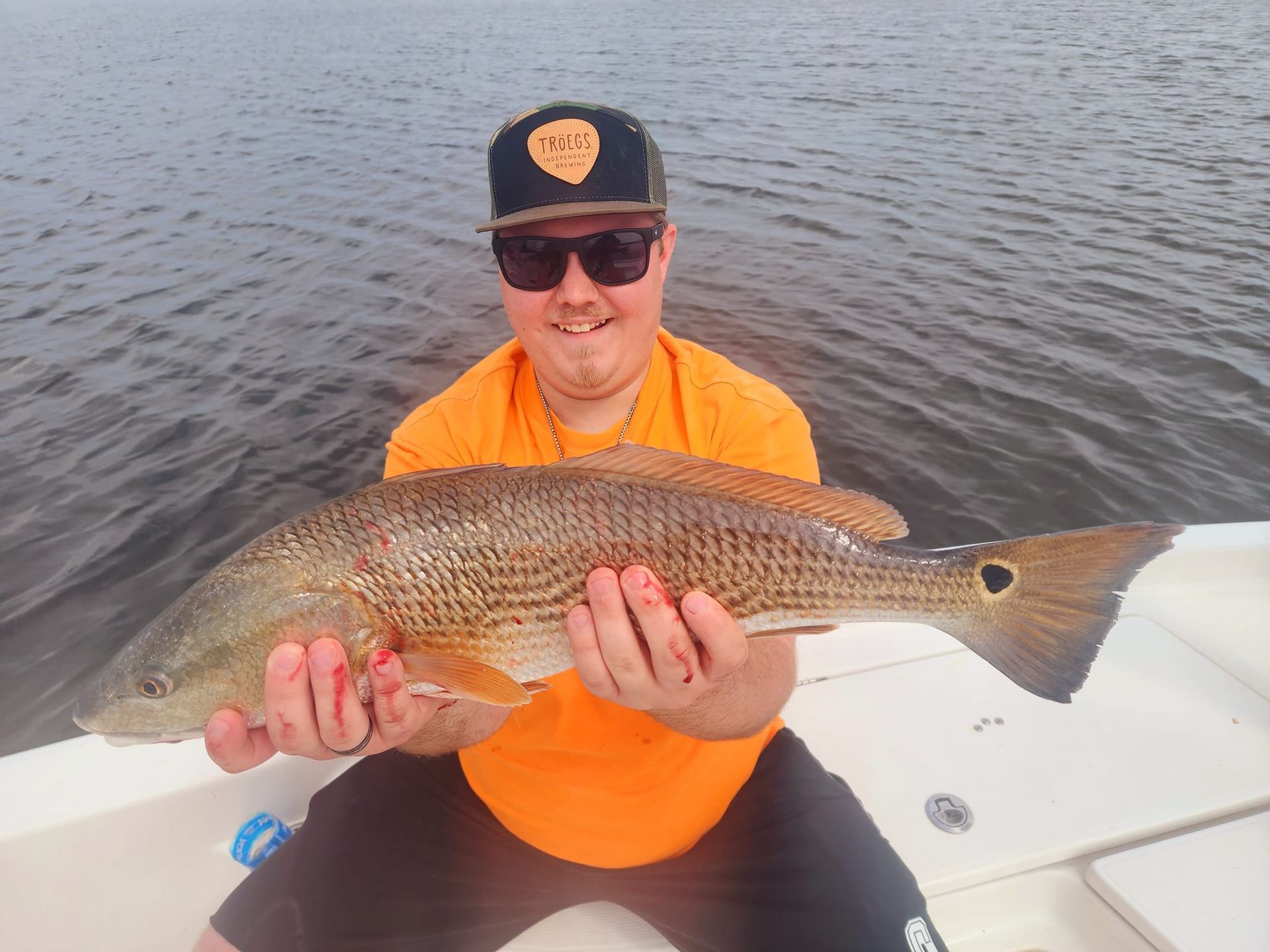 Man holding a large redfish, smiling, on a boat, with dark water in background.