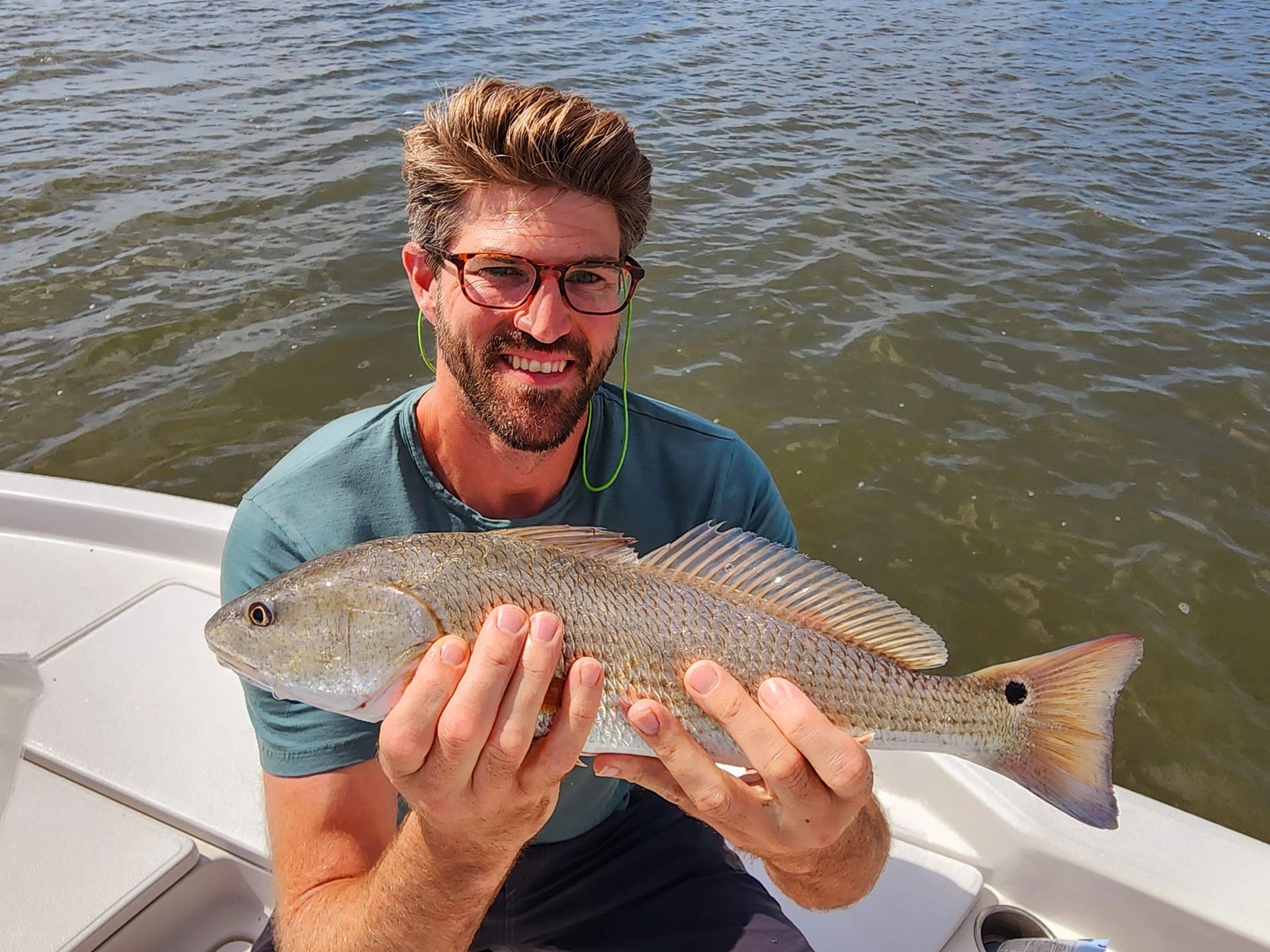 Man smiling, holding a redfish on a boat, water in background.