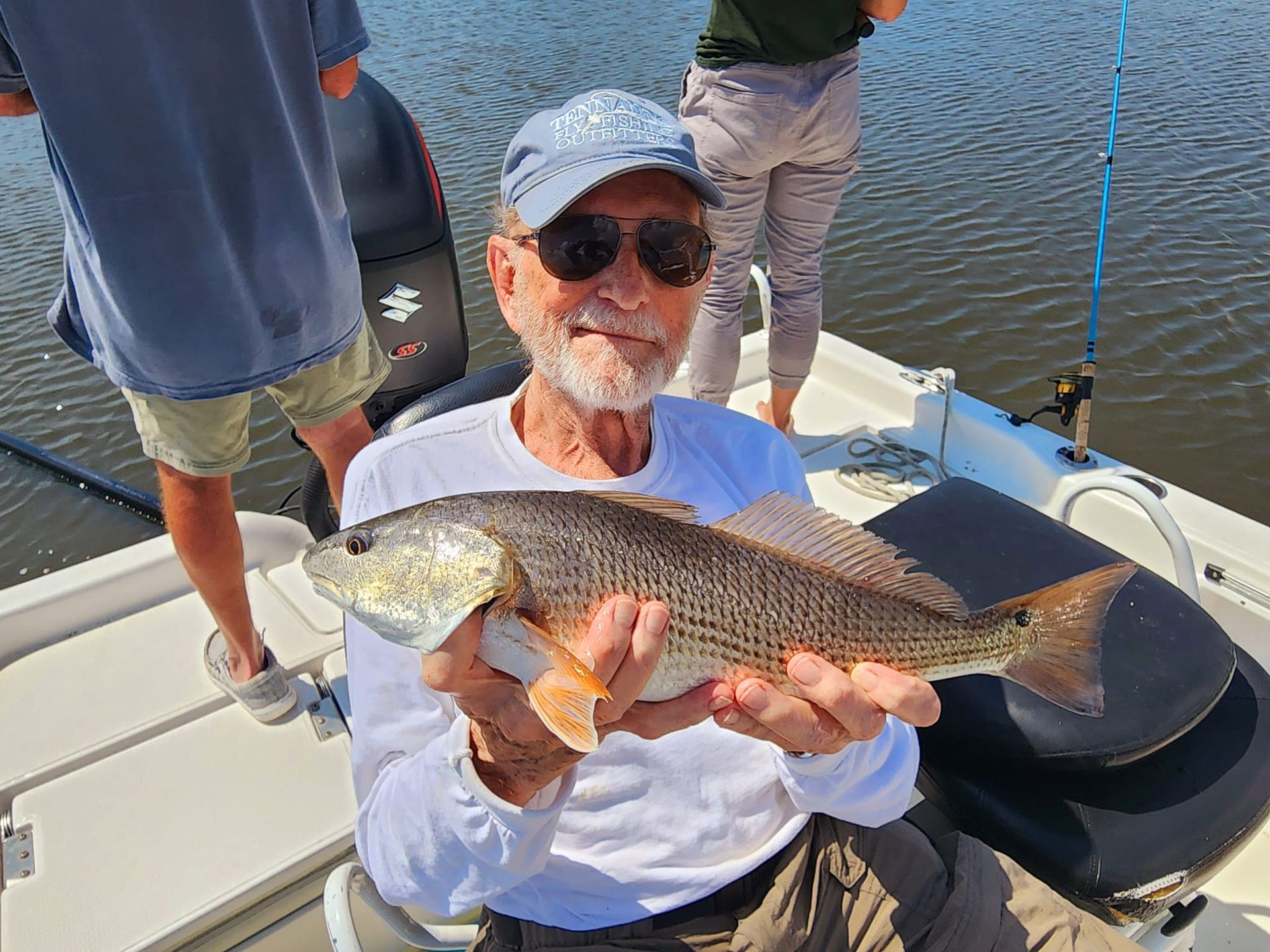 Man holding a redfish on a boat, smiling; other people visible in background.