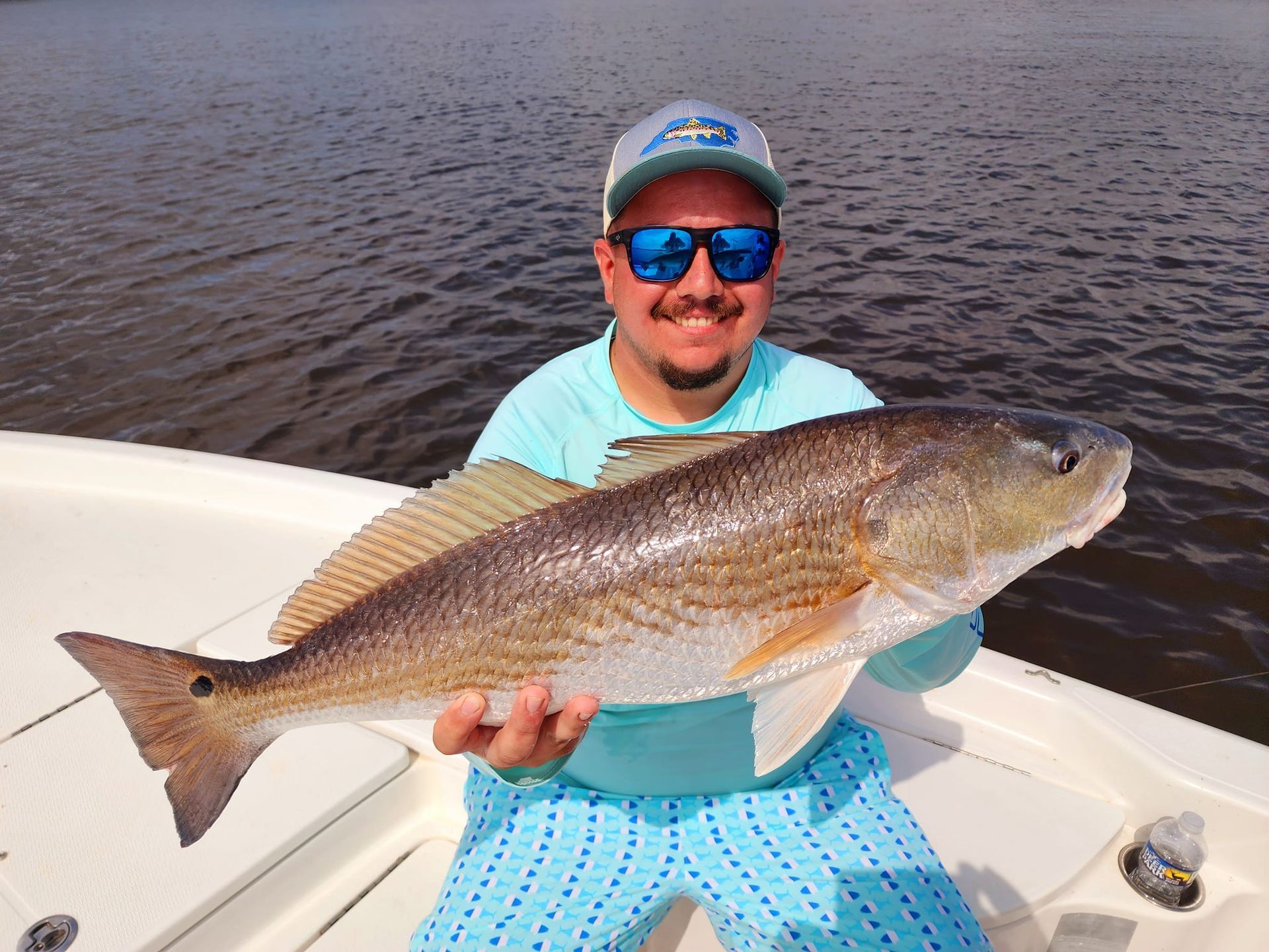 Man on boat smiling, holding a large redfish. Water and sky visible in the background.