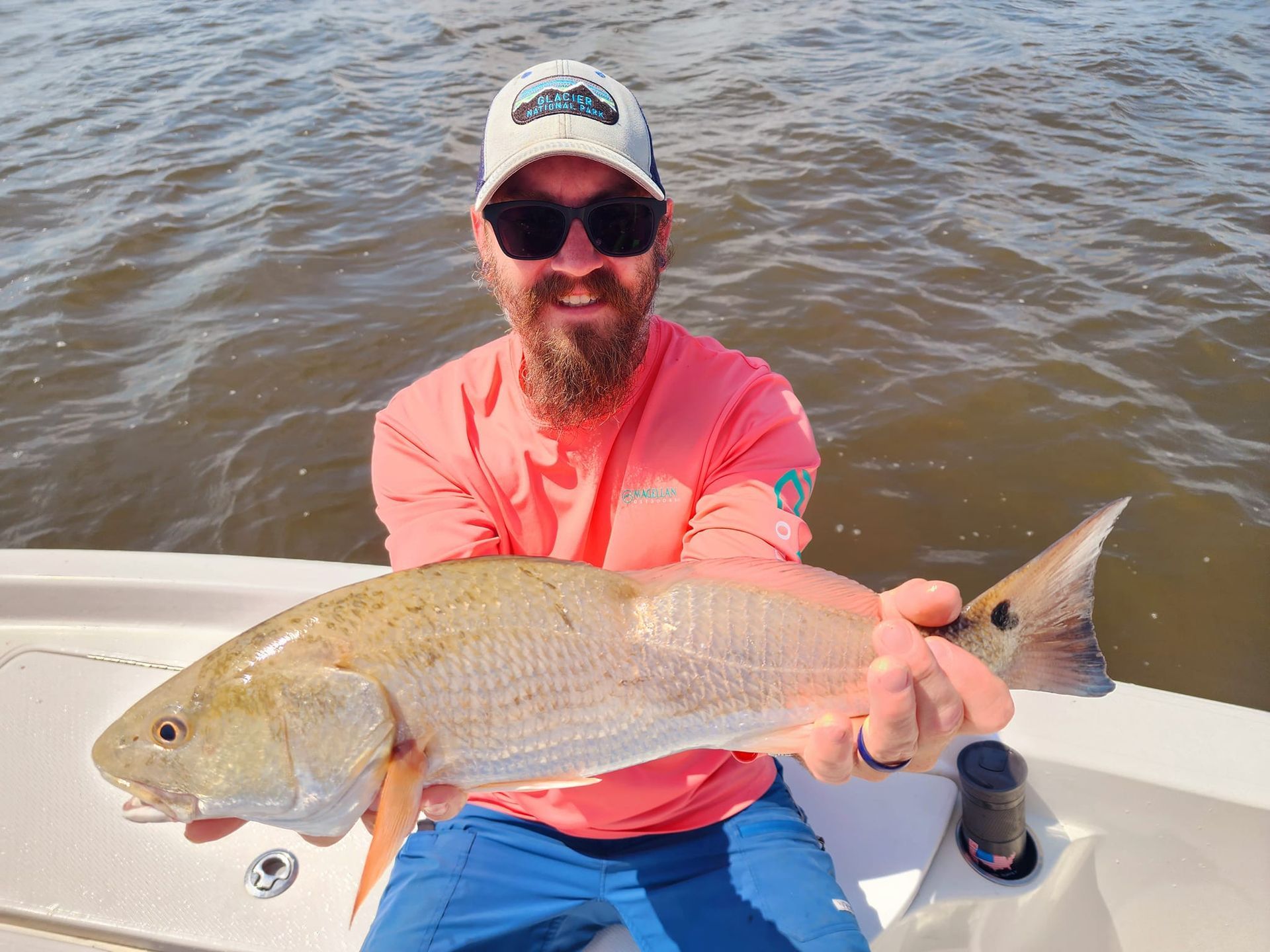 Man on a boat holding a large redfish. He is smiling. The water is visible.