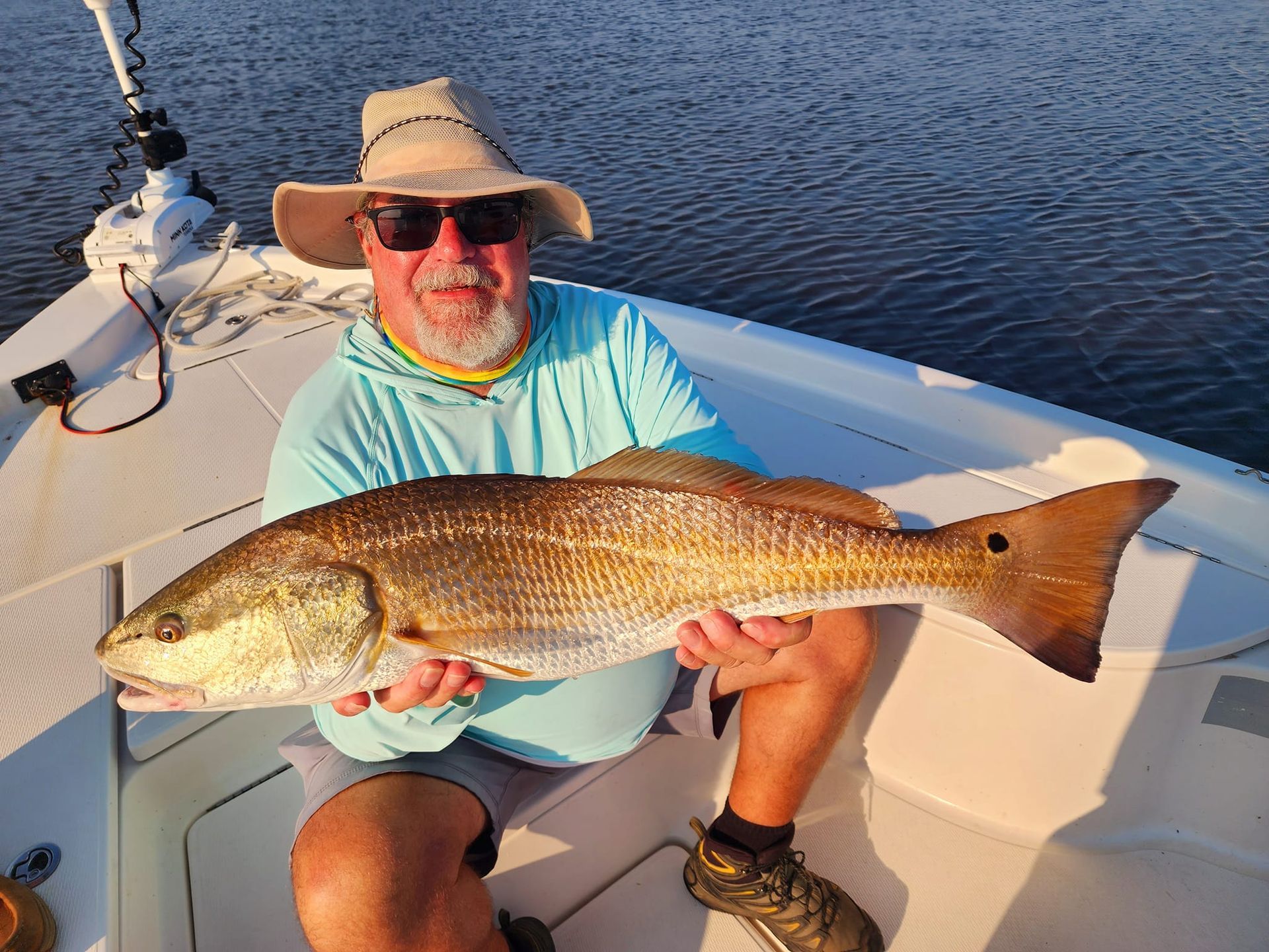 Man holding a large redfish on a boat; sunlight, blue water.