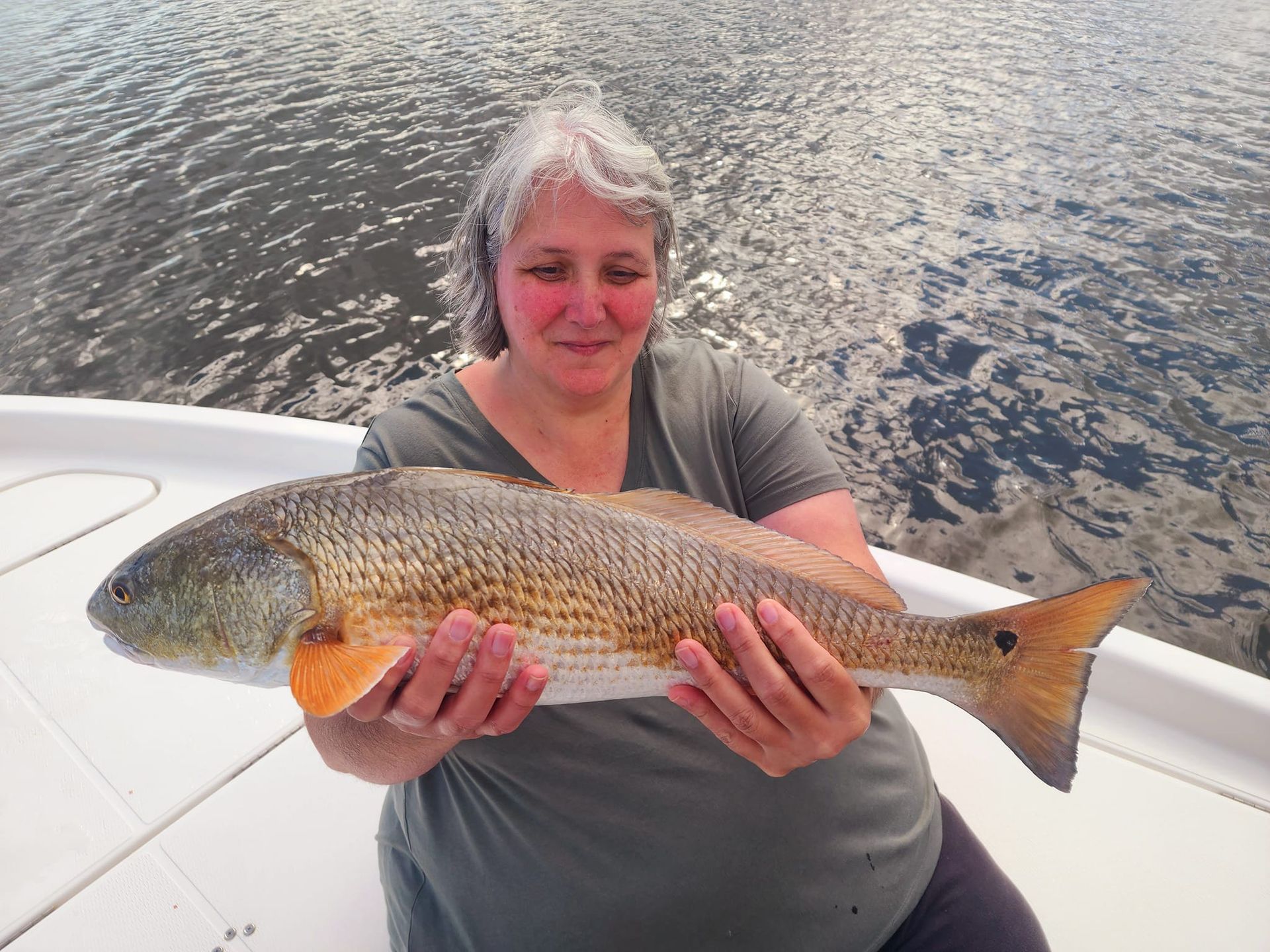 Woman holding a large redfish on a boat; water in the background.