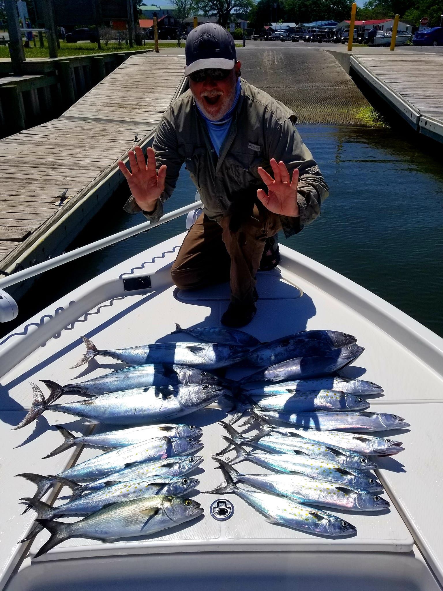 Man kneels in boat, displaying a large catch of fish. Outdoors, sunny day.