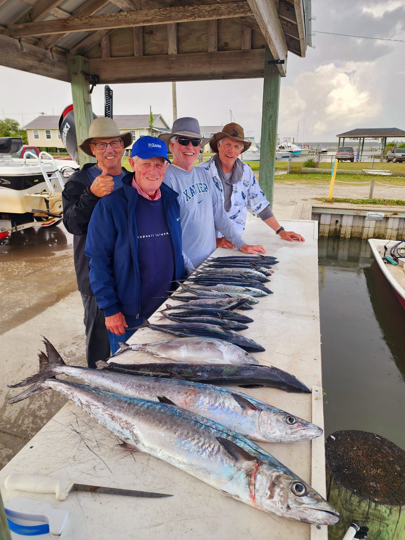 Four men pose with a row of fish on a dock table. Two larger fish are in the foreground.