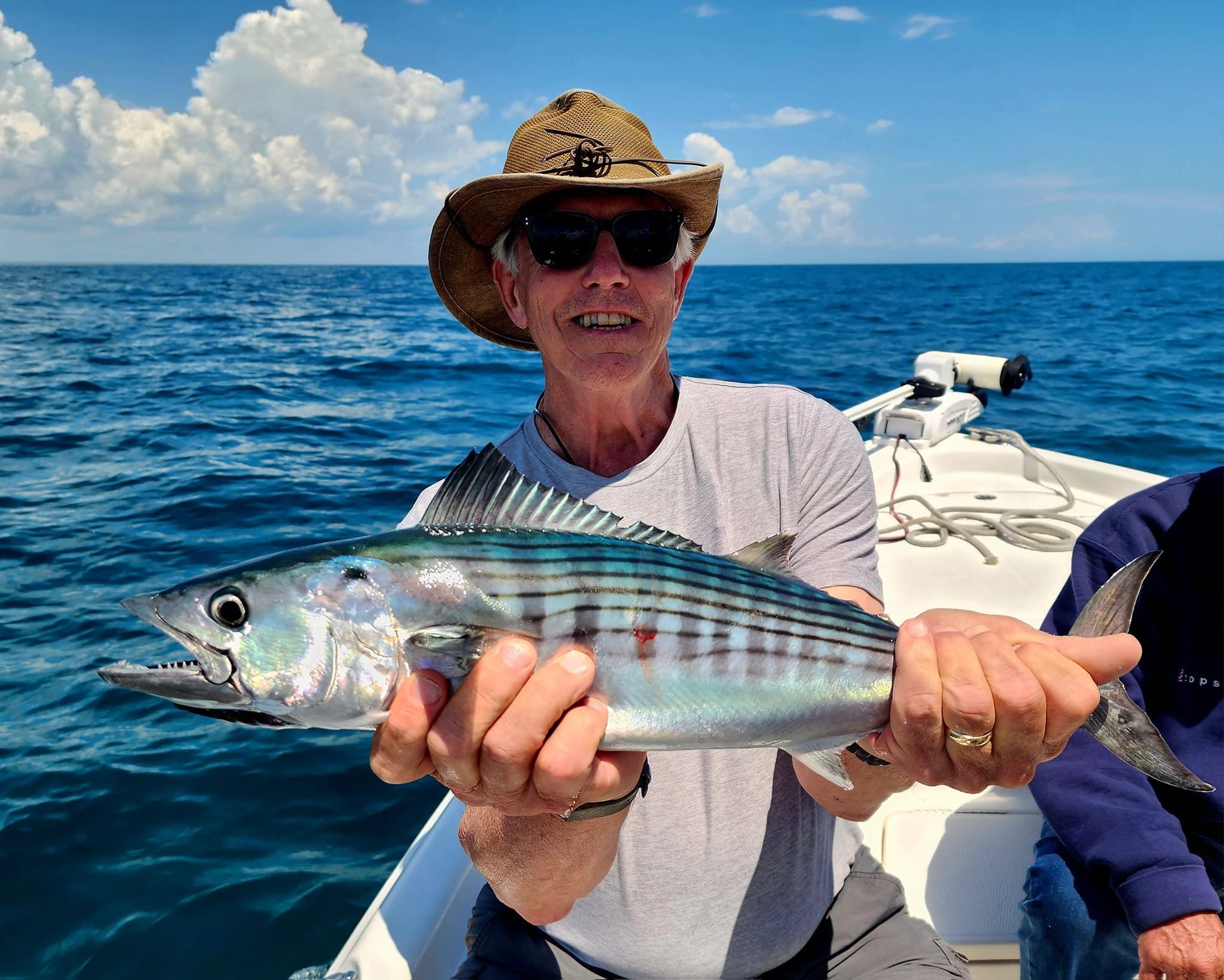 Man on boat holding up a fish, ocean in background.