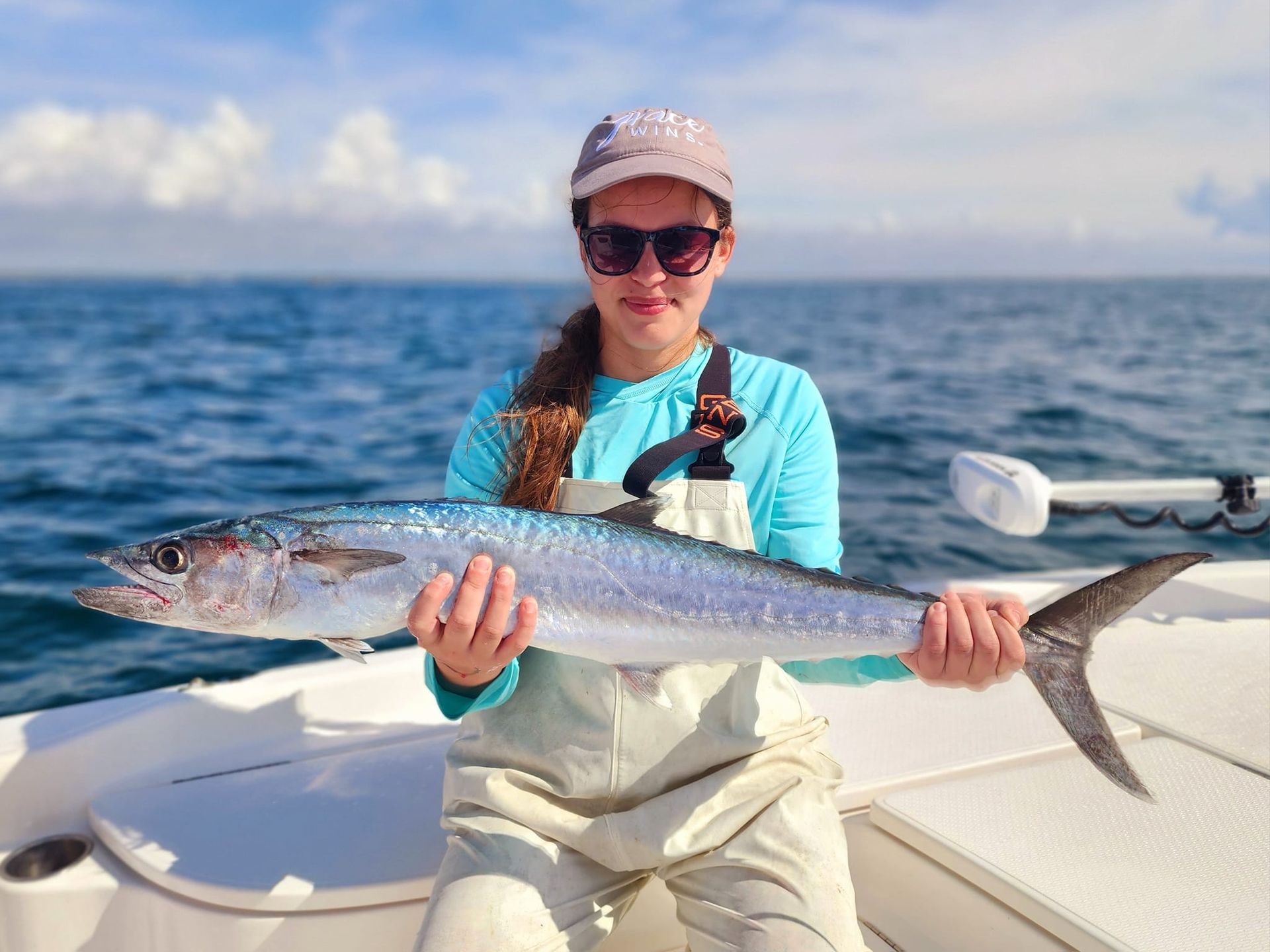 Woman on a boat holding a large fish, blue water in background.