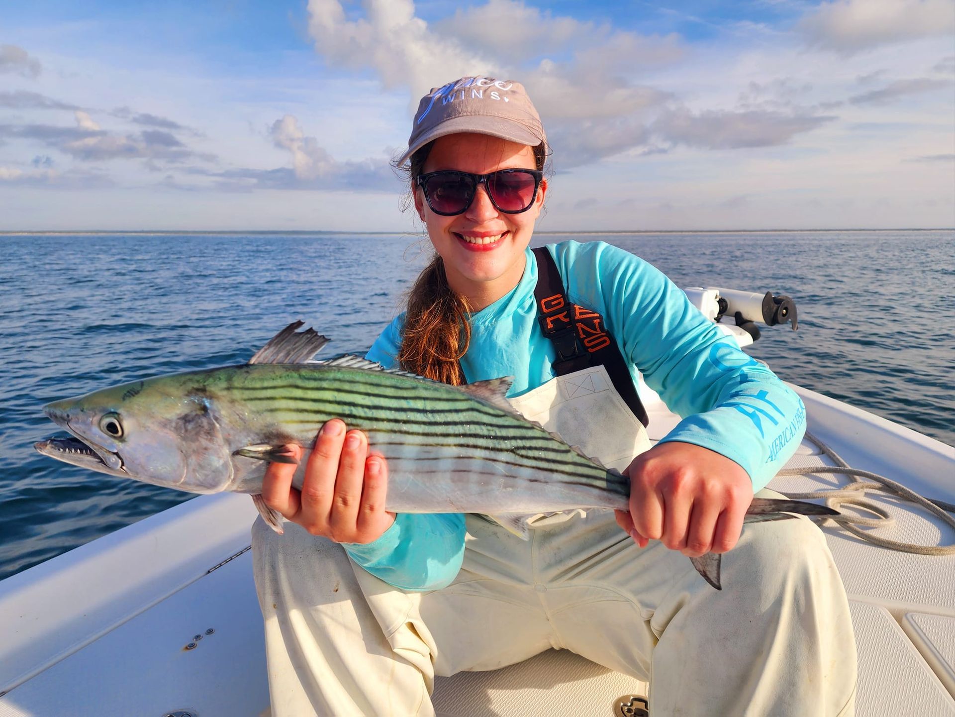 Woman on boat holding a striped fish; ocean background.