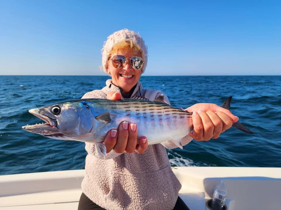 Woman smiling, holding a fish on a boat; blue sea and sky background.