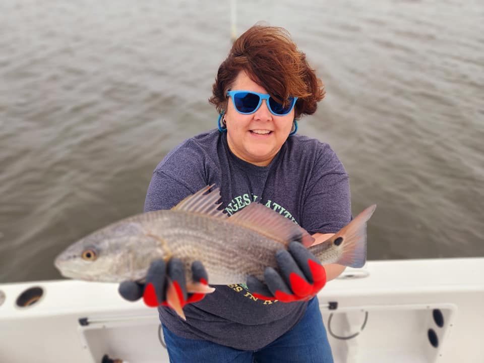 Woman wearing sunglasses holds a redfish on a boat, smiling at the camera. Water in background.
