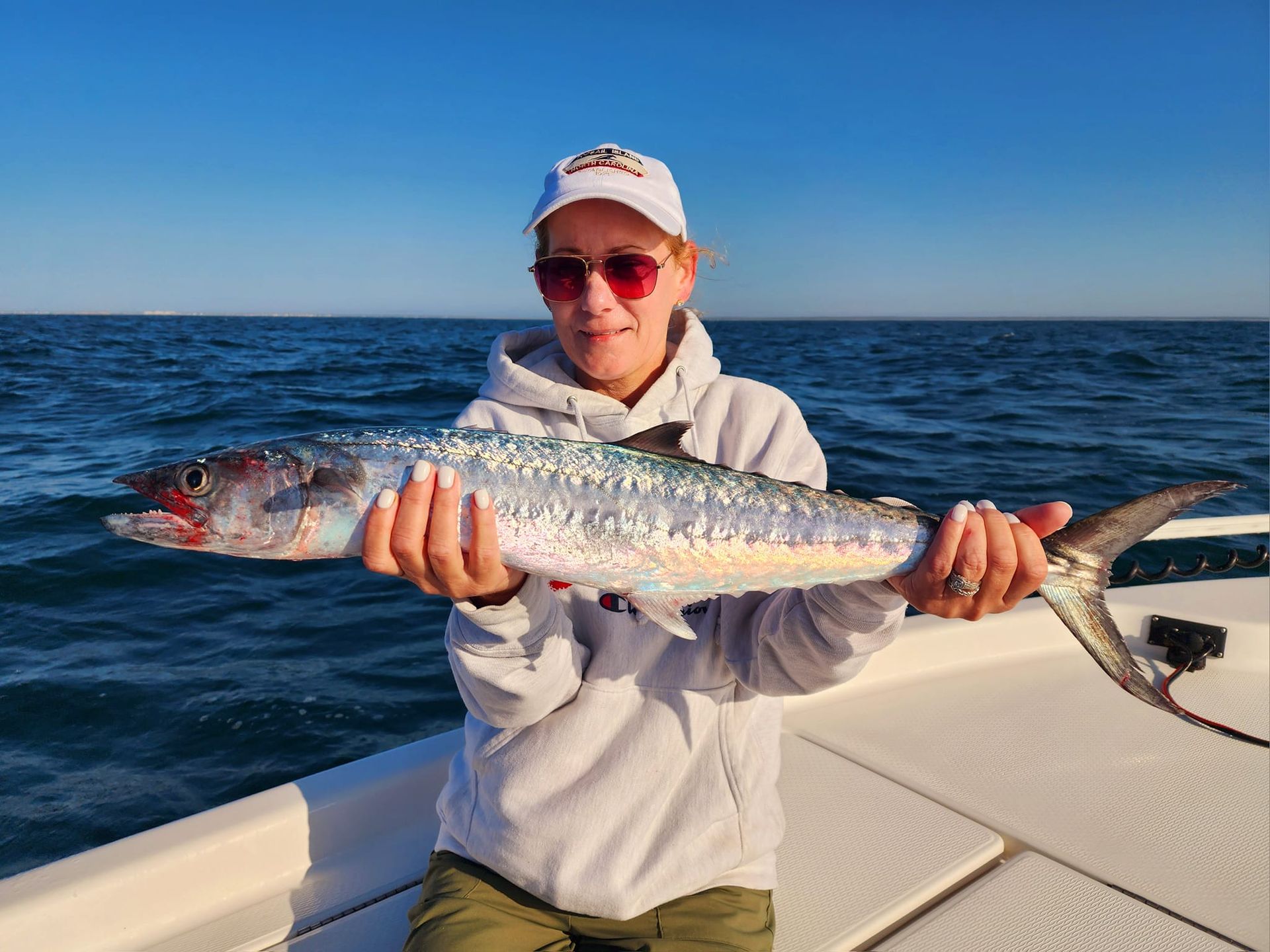 Woman on a boat holding a large fish, blue water in the background.