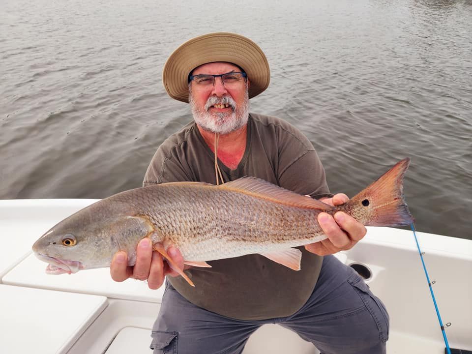 Man in hat holding a large redfish on a boat, near water.