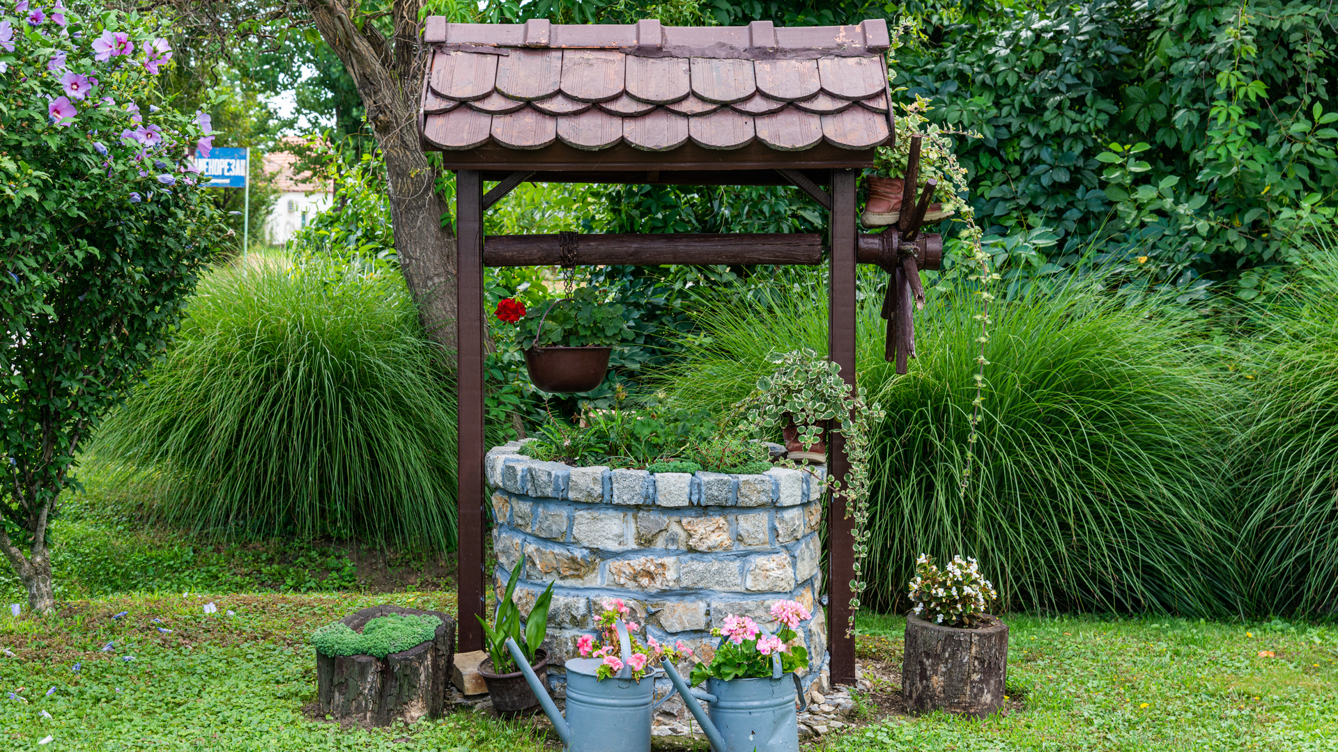 A stone well with a watering can and potted plants in a garden.