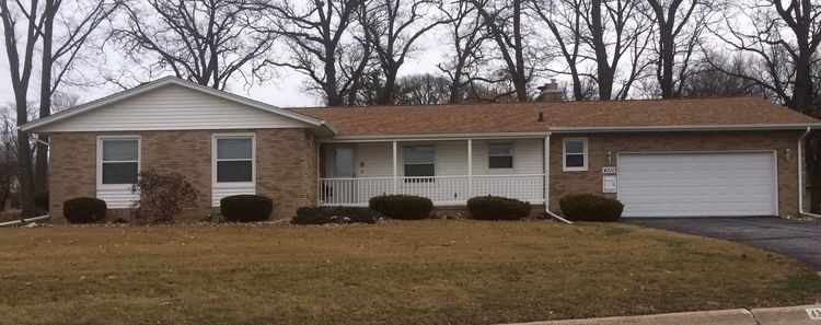 Ranch-style house with brick facade, brown roof, white garage door, and leafless trees in the background.