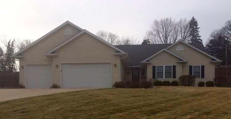 Beige ranch-style house with a two-car garage, black shutters, and a brown lawn.