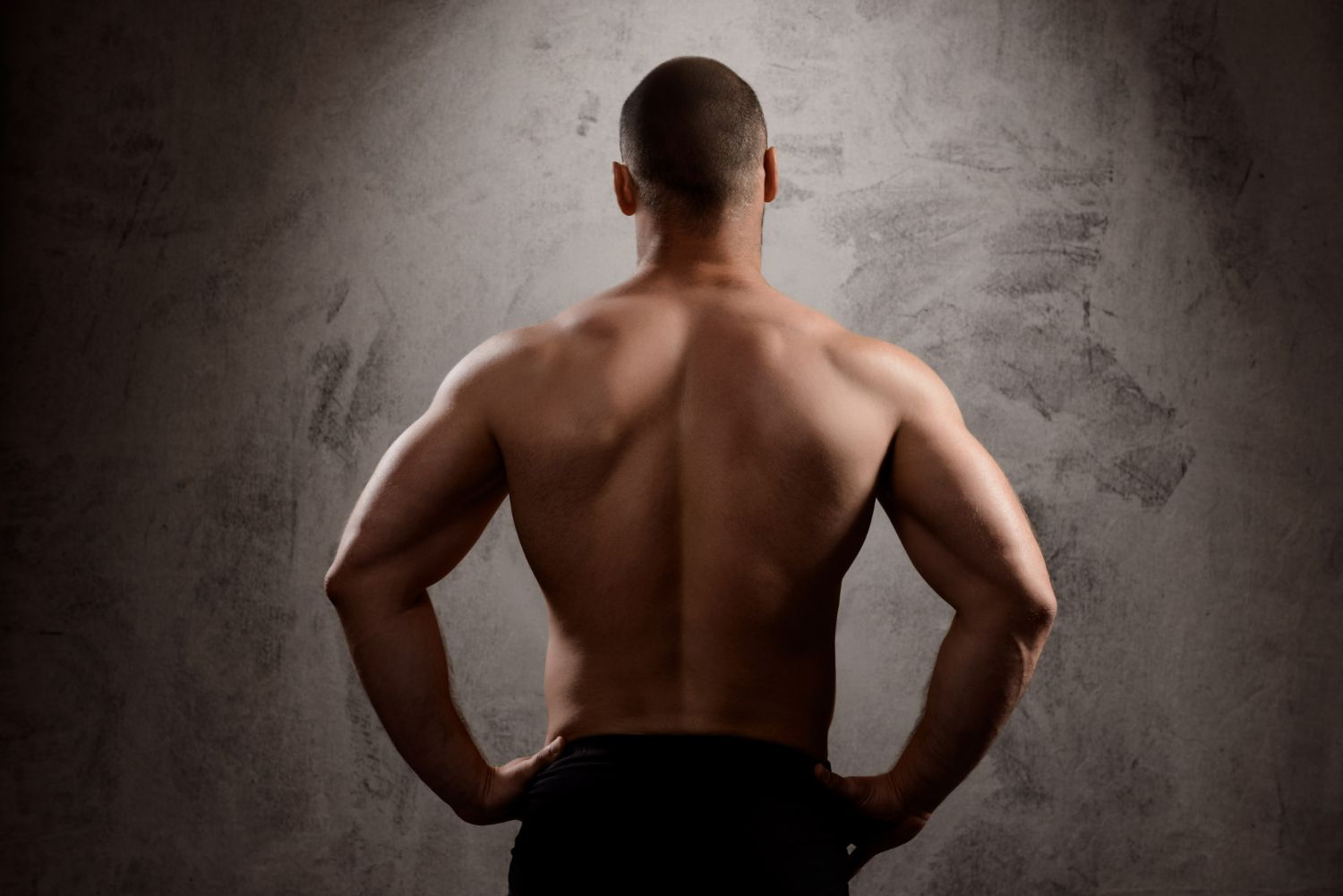The back of a shirtless man standing with his hands on his hips.