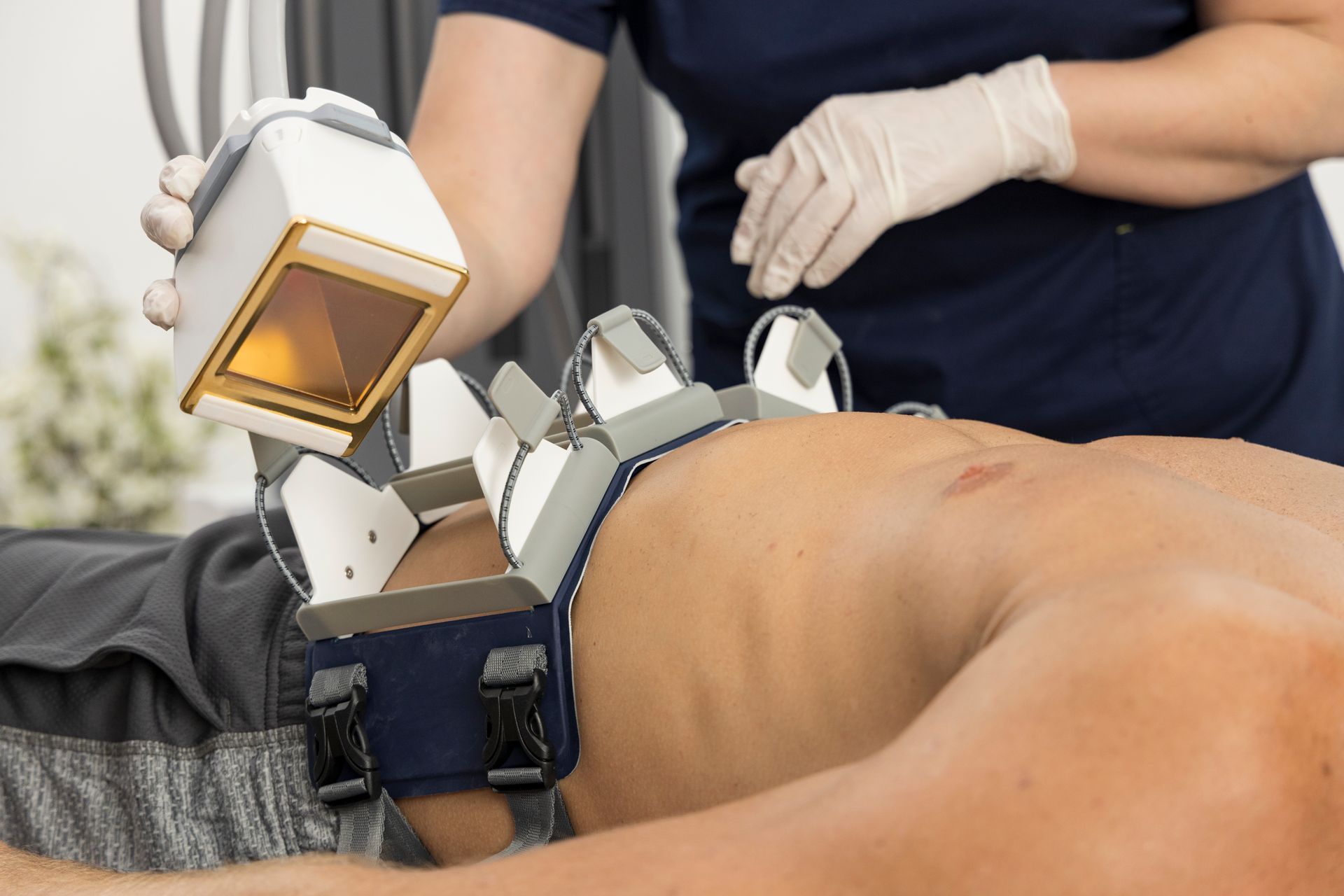 Person receiving a body treatment. A technician applies a device to their back, held by a securing strap.