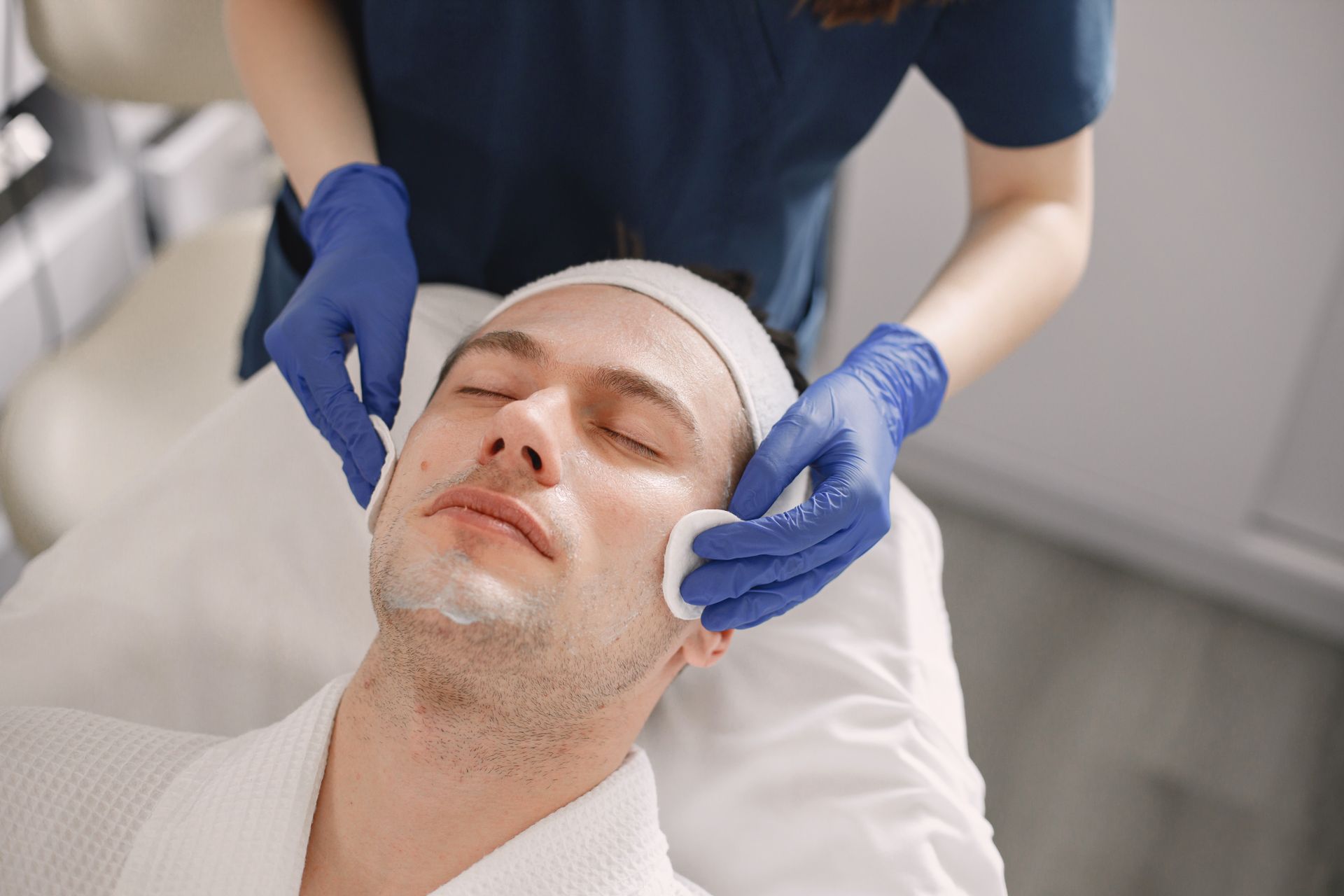 Person receiving facial treatment, being wiped with cotton pads, in a spa setting.
