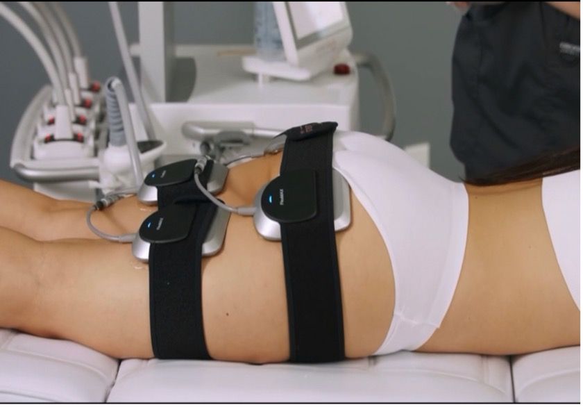 A woman is laying on a bed with a machine on her back.