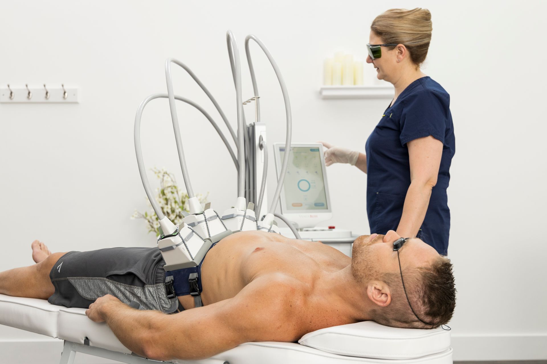 A man is laying on a bed getting a laser treatment from a woman.