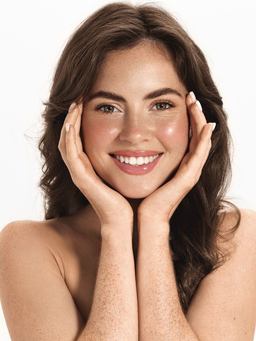 A woman is smiling with her hands on her face.