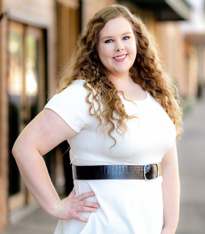 Woman in a business suit with arms crossed, smiling confidently, in a modern office.