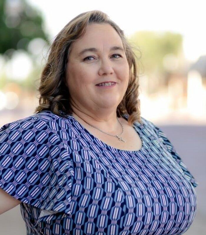 Portrait of a smiling person in a blue patterned blouse outdoors with a blurred background